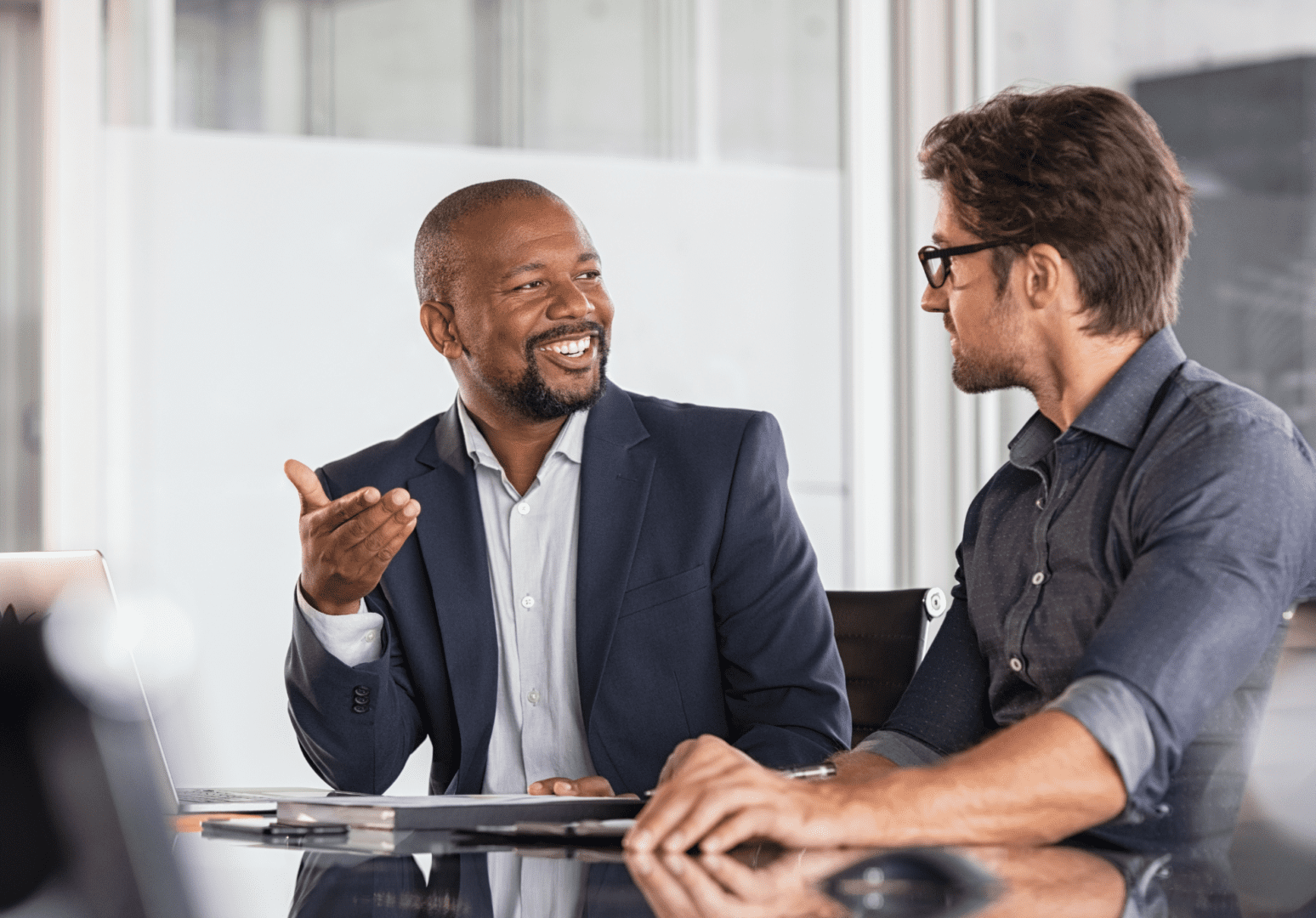 Two men sitting at a table talking to each other.